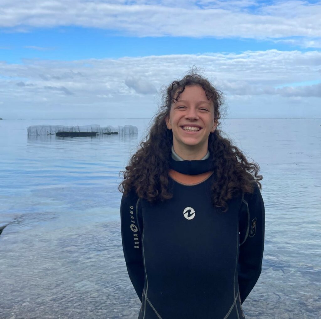 Portrait de Camille Dervillez devant la cage expérimentale des oursins dans le lagon de Vairao © Maëlys Chapis